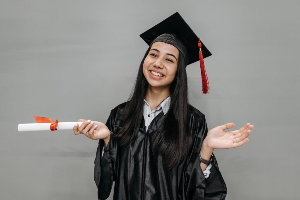 Young woman in graduation gown and cap, smiling and holding diploma. Studio portrait capturing academic success.